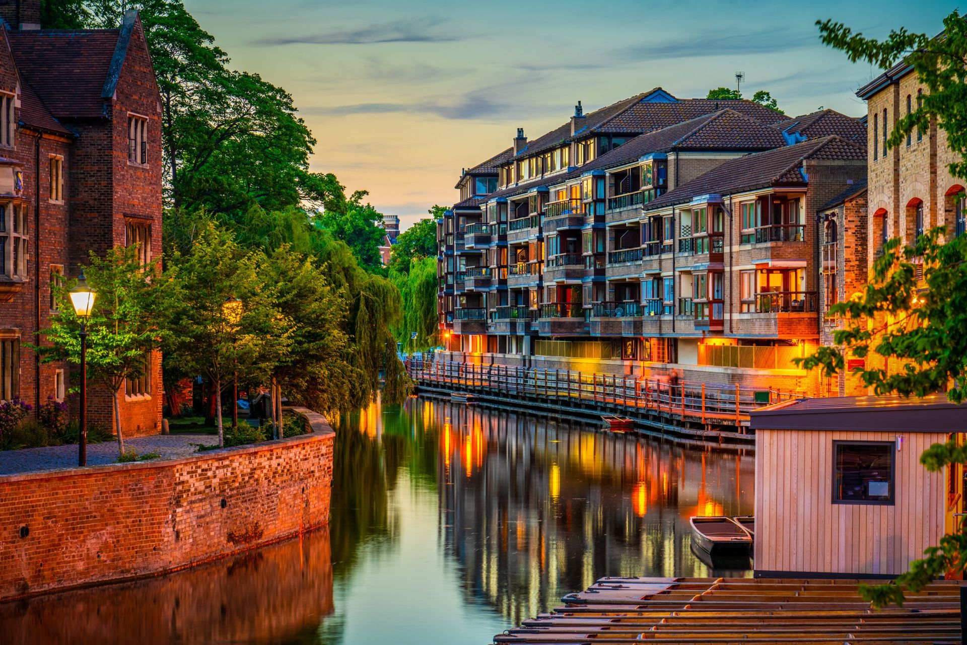 Canal with buildings, trees, and reflections at dusk; warm lighting.
