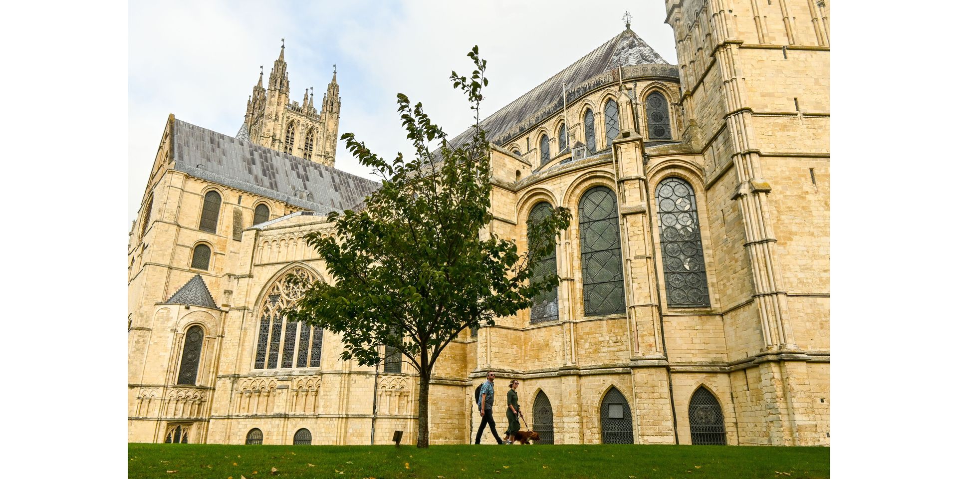 Canterbury Cathedral with a small tree in front. Two people are walking in the lower-center.