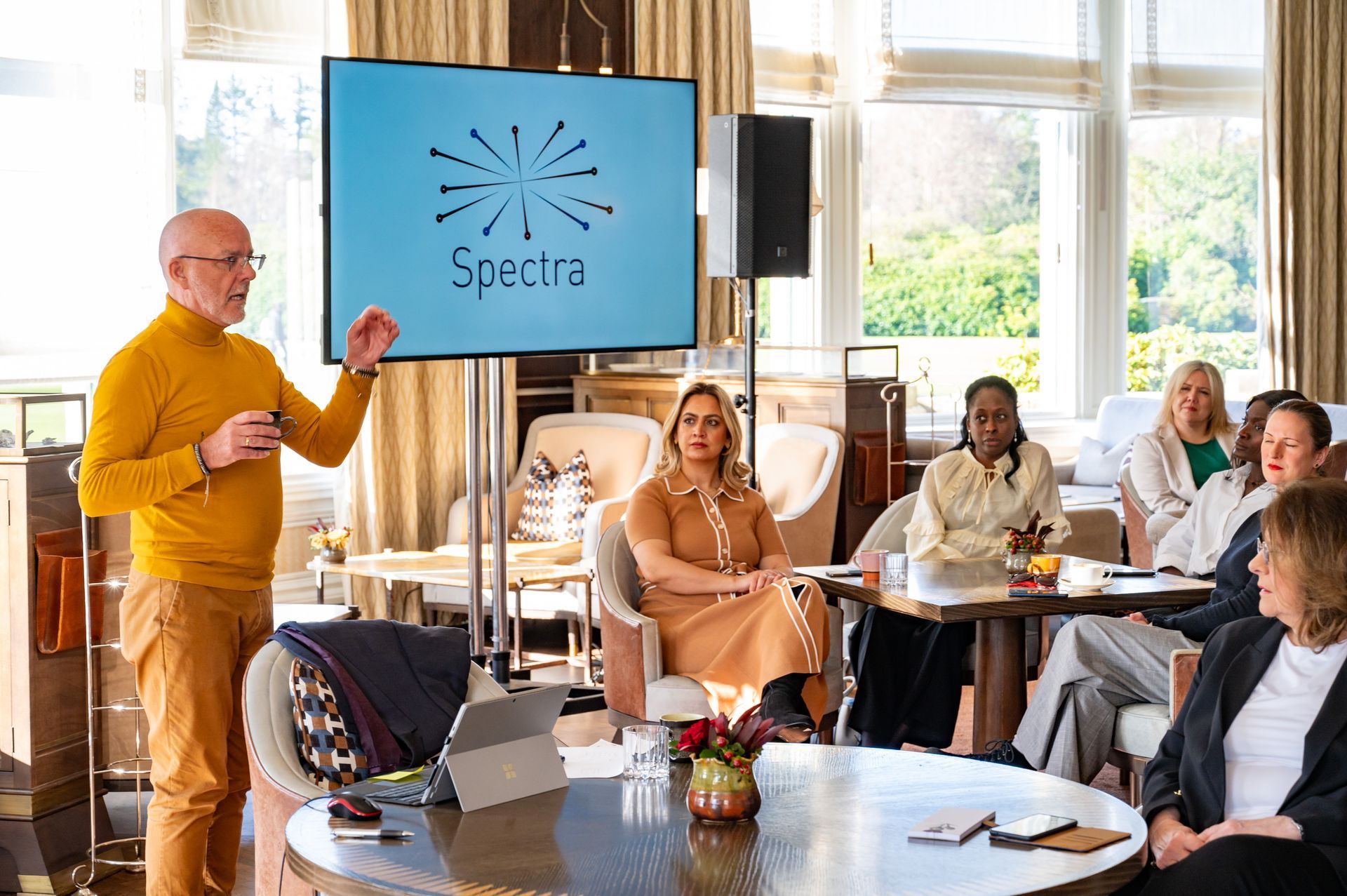 Man presenting to a group seated around a table; screen with