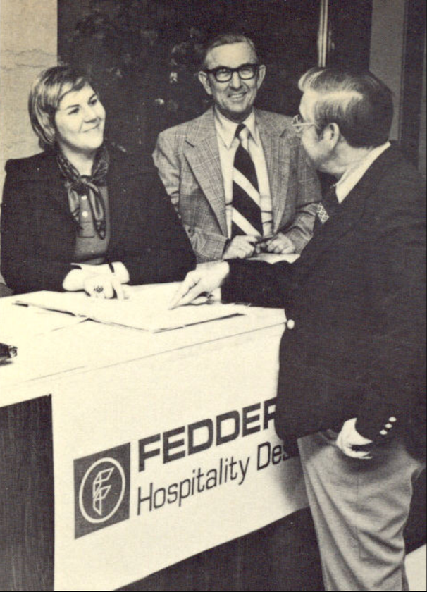 People at a Fedder Hospitality Design table. A man points to papers as others smile, one with glasses.