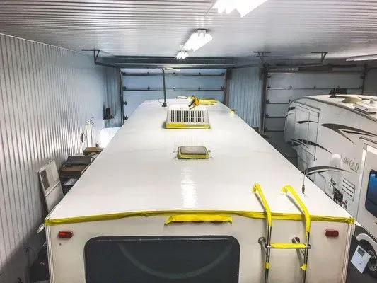 Toit de camping-car blanc à l'intérieur d'un garage, entouré de murs, avec échelles et évents visibles.