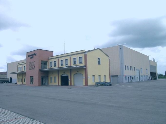Grande edificio industriale con facciata beige e rosa sotto un cielo nuvoloso.
