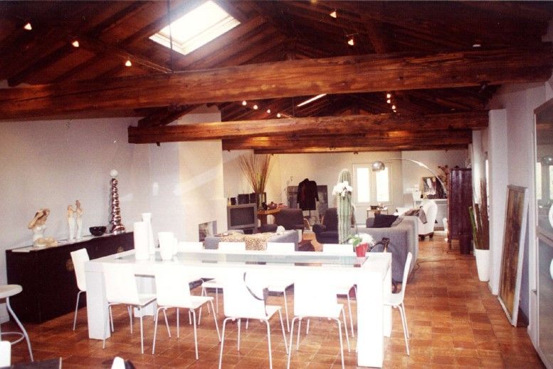 Ampia camera con tavolo e sedie bianchi, travi in legno a vista e lucernario.