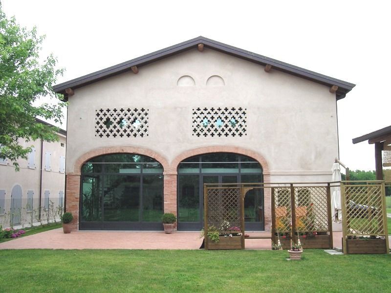 Edificio color marrone chiaro con porte ad arco in vetro, ritagli decorativi in pietra, tetto marrone e prato erboso.