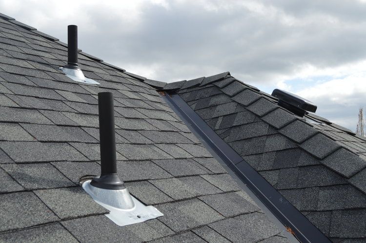 A roof with two chimneys on it with a cloudy sky in the background