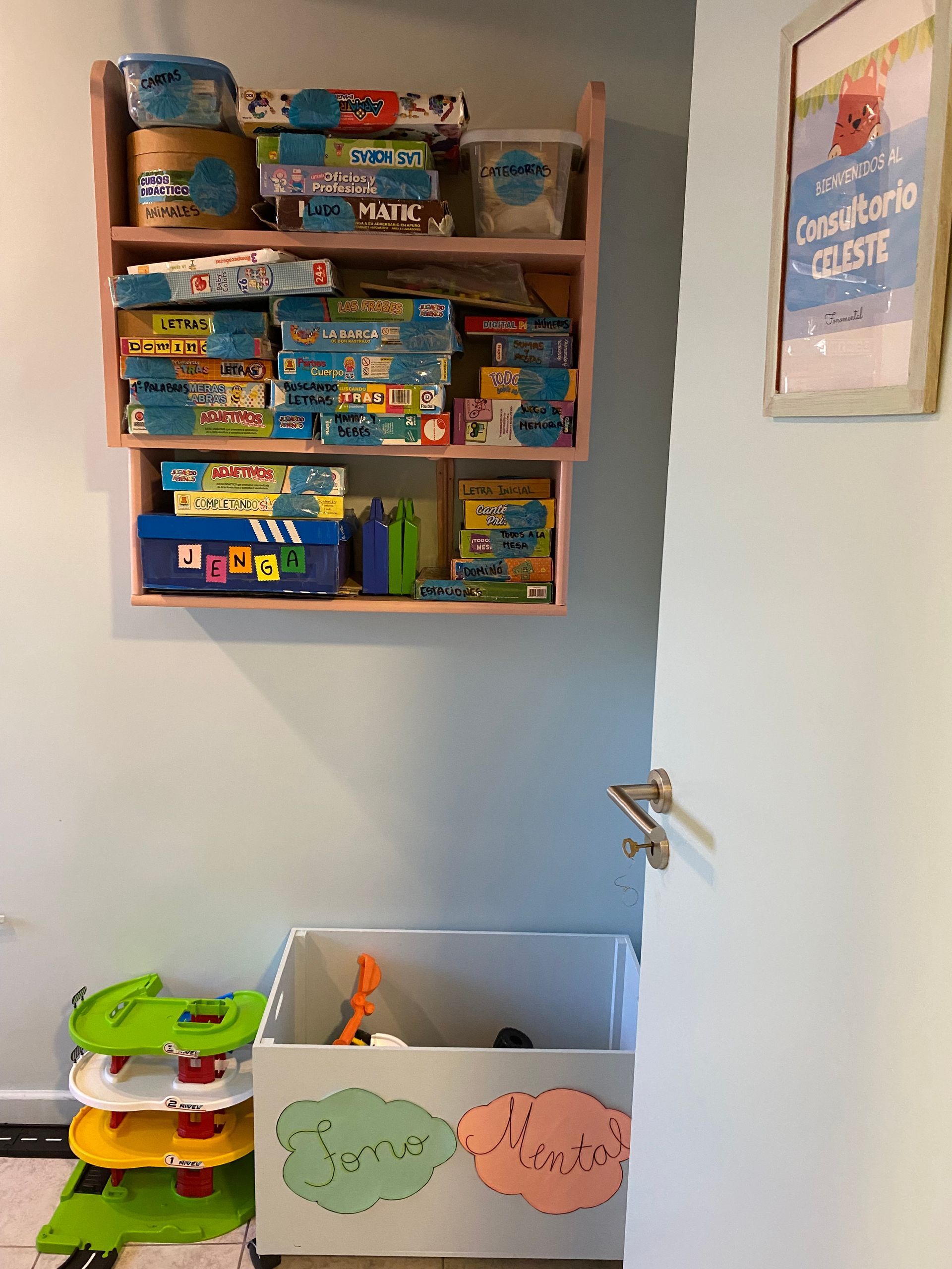 Estanterías con juegos de mesa, un baúl de juguetes y un zapatero contra una pared azul pálido.
