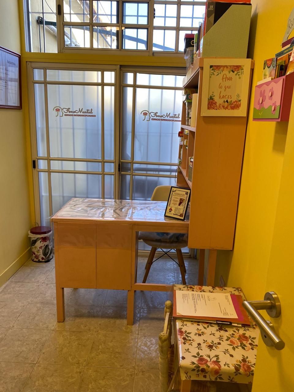 Pequeña oficina con escritorio, silla y librero. Puerta de cristal esmerilado que da al exterior.