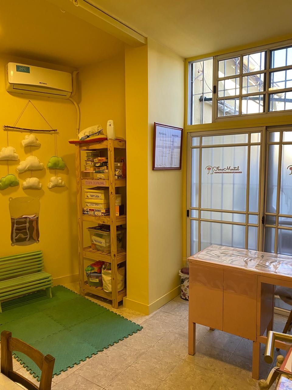 Habitación de paredes amarillas con un banco, estantería, mesa y aire acondicionado. 