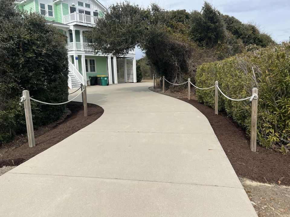 Concrete path leads to a beach house with a rope fence and landscaped edges.