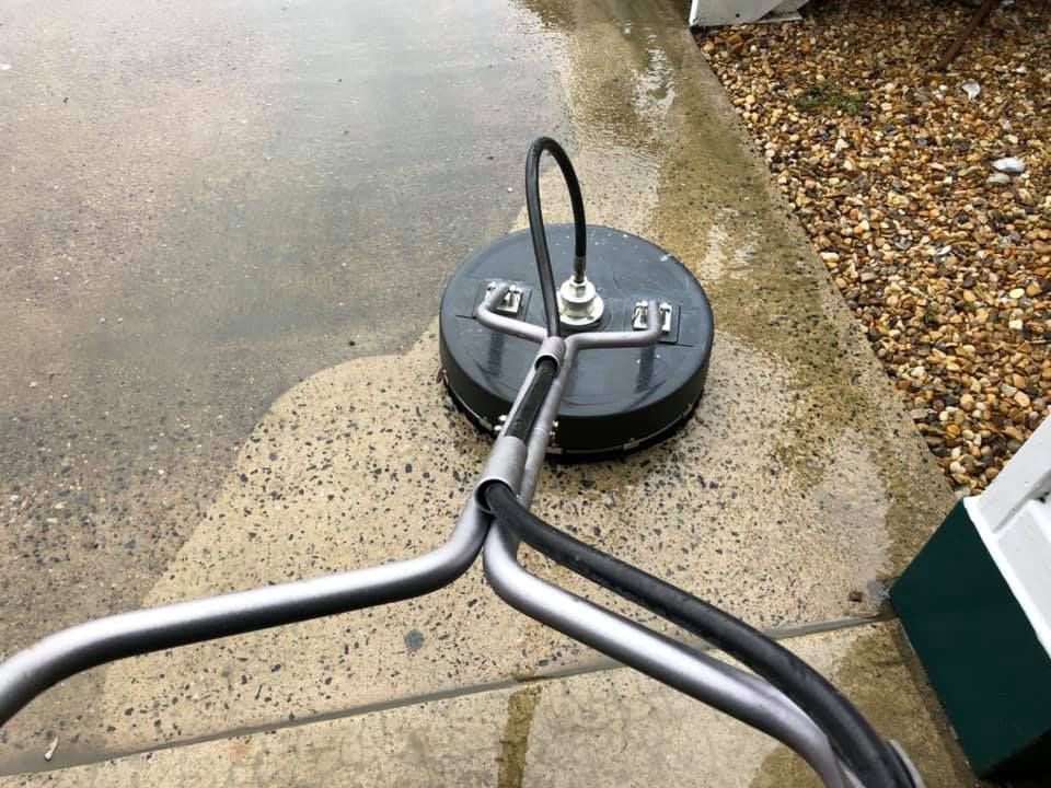A person power washing a concrete driveway with a spinning surface cleaner.