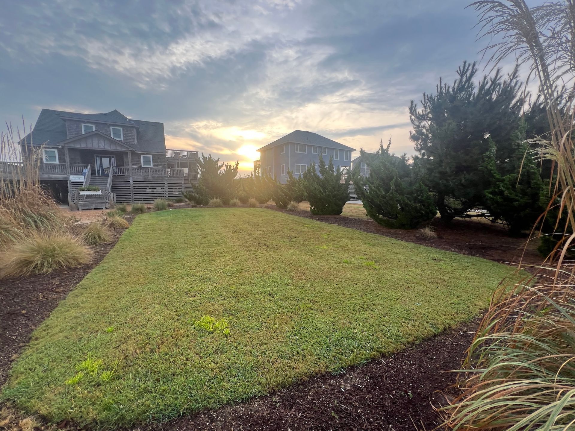 A green yard with buildings and trees under a cloudy sky at sunset.