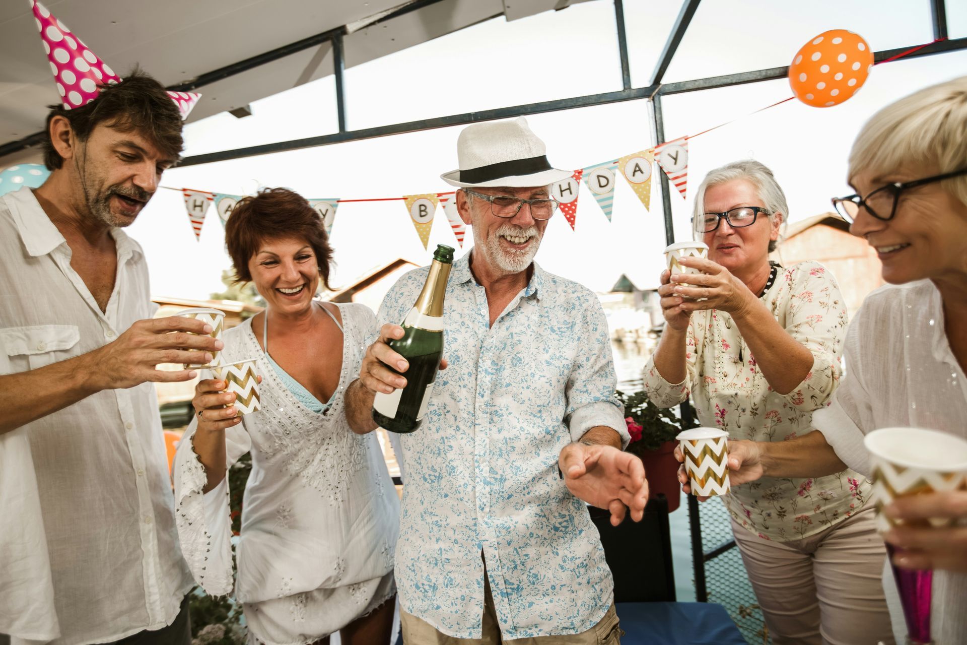 Group of friends toasting with drinks at a festive outdoor party, smiling under colorful decorations