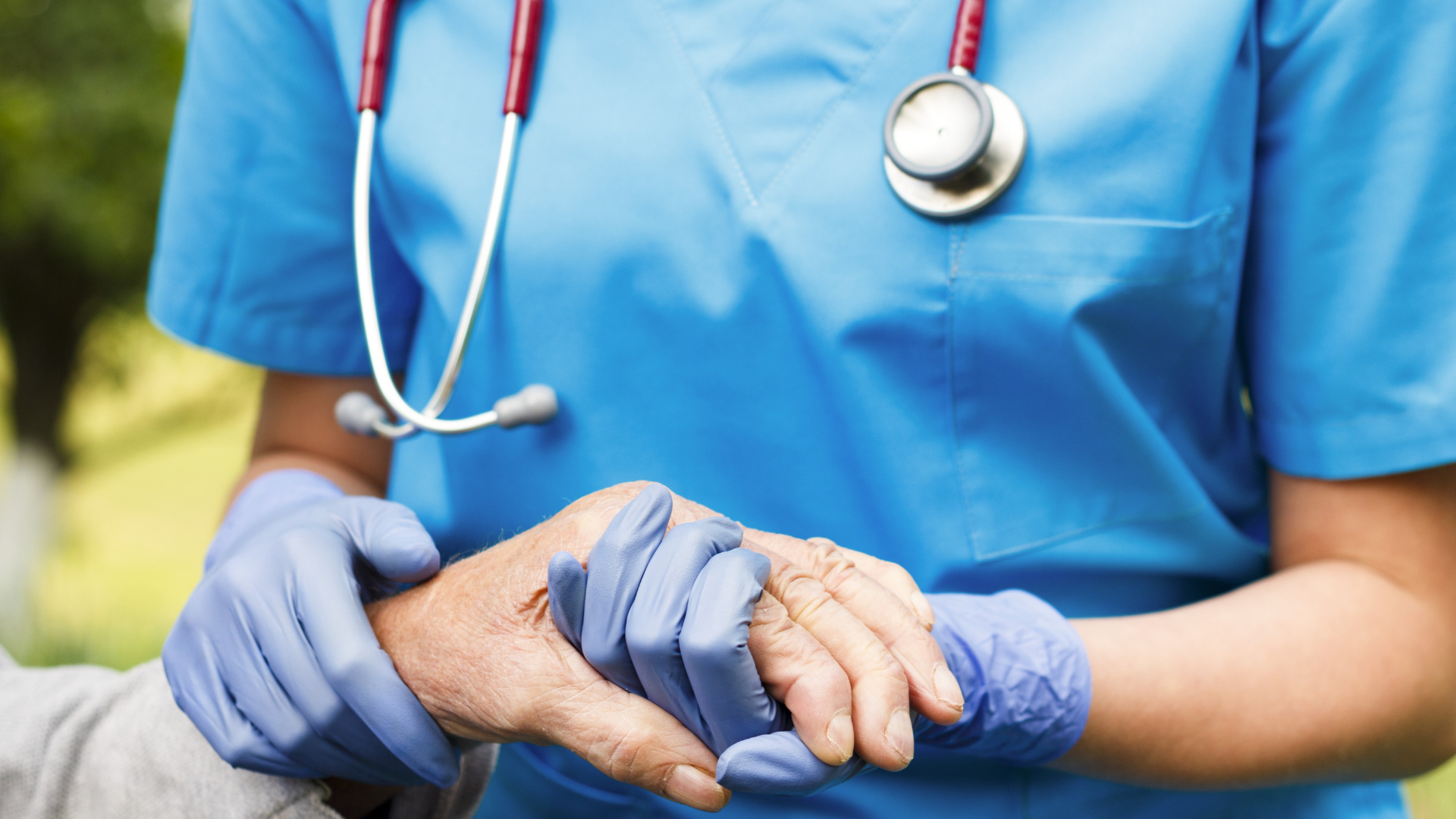 A nurse is holding the hand of an elderly woman.