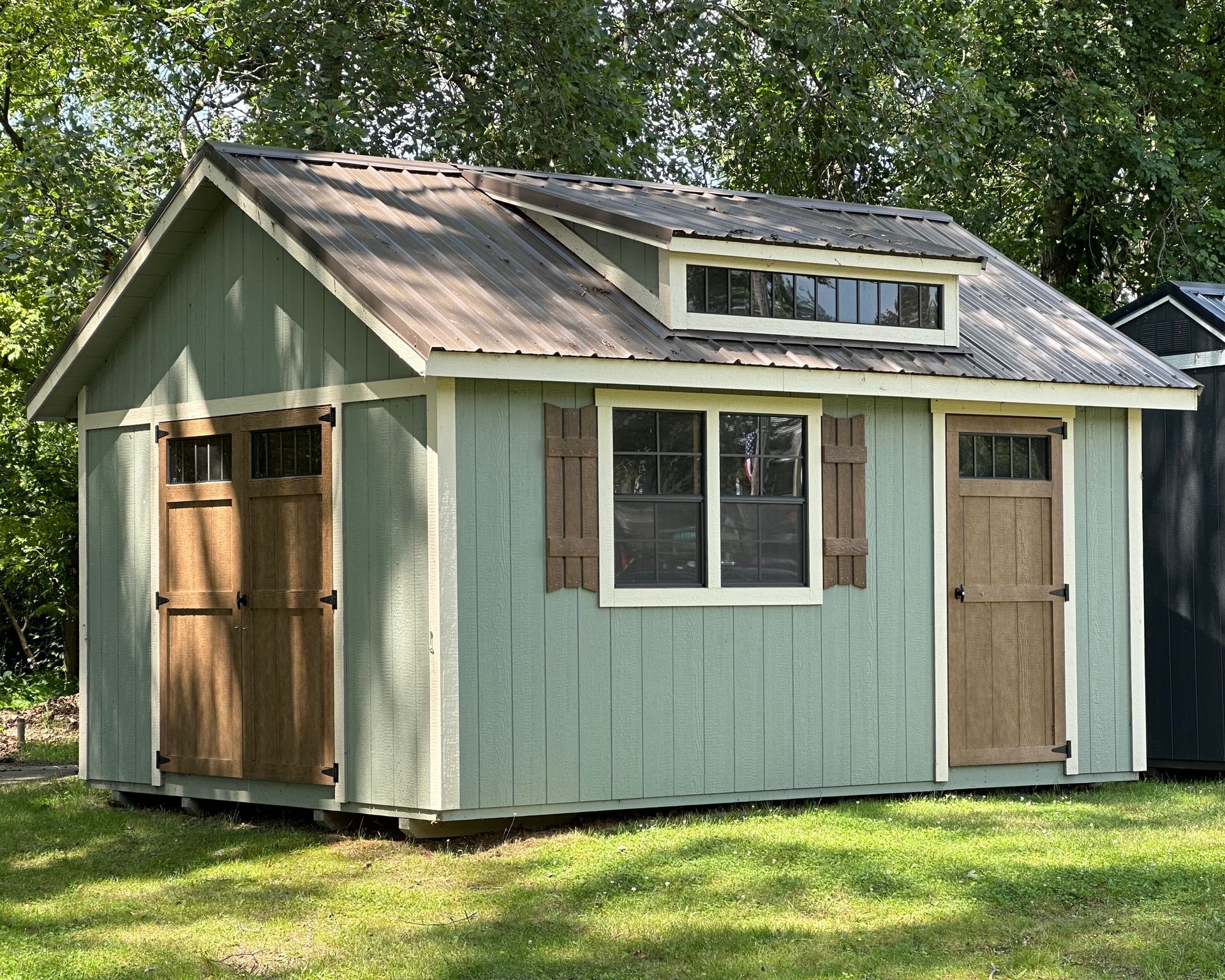 A small green shed with a window on the roof is sitting in the grass.