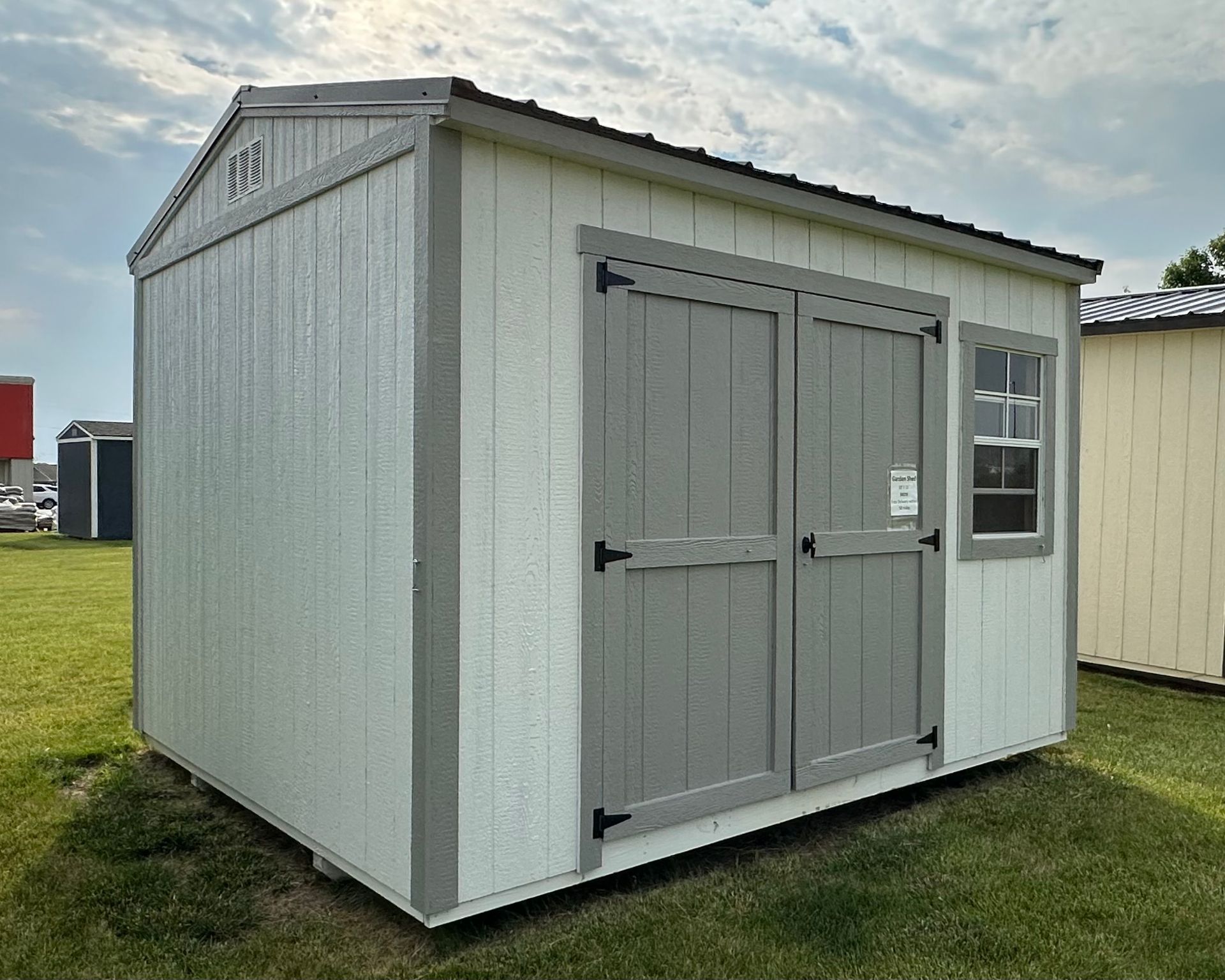 A white and gray shed is sitting in the middle of a grassy field.