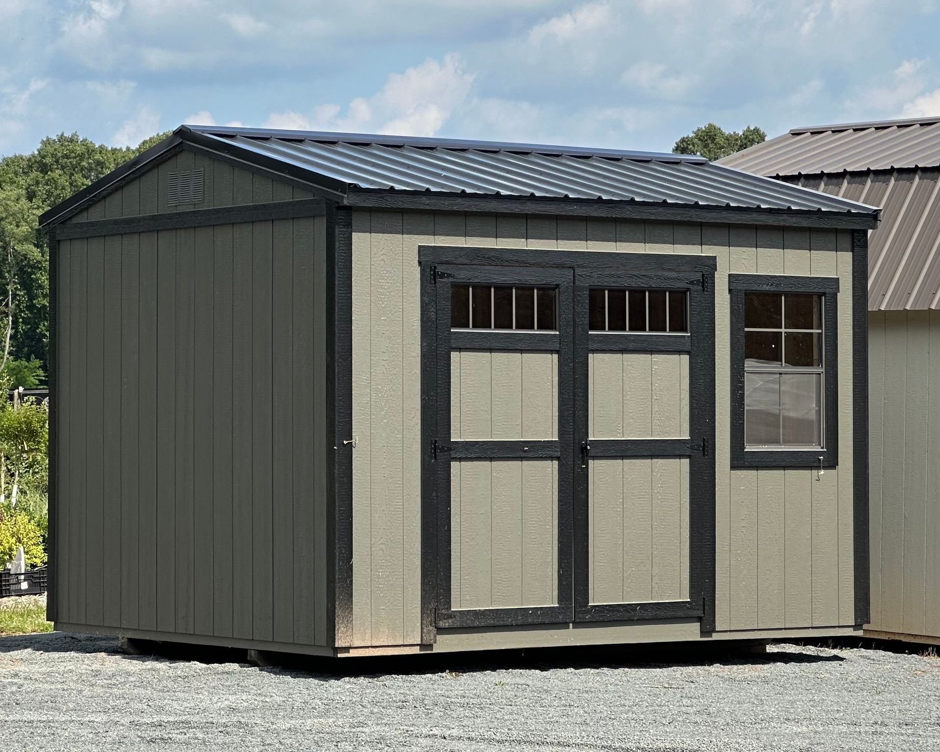 A small shed with a black roof is sitting in a gravel lot.