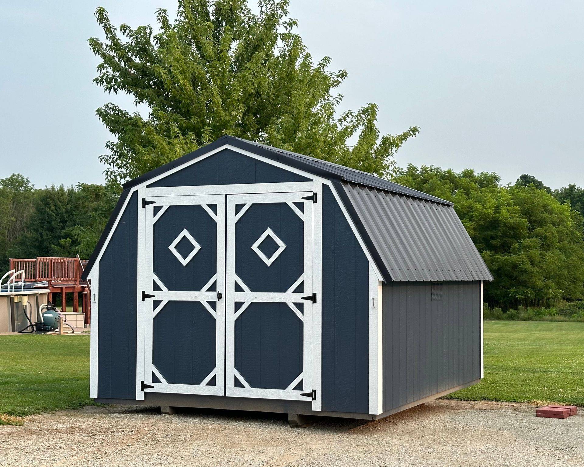 A black and white barn shed is sitting in the middle of a grassy field.