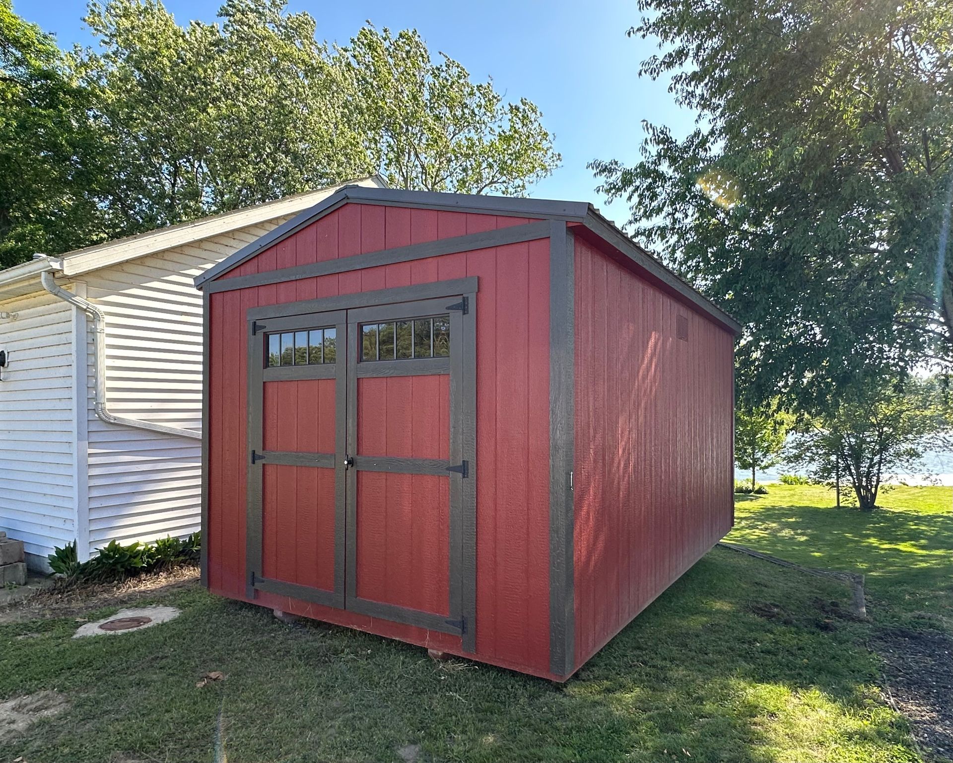 A red shed is sitting in the grass next to a white house.