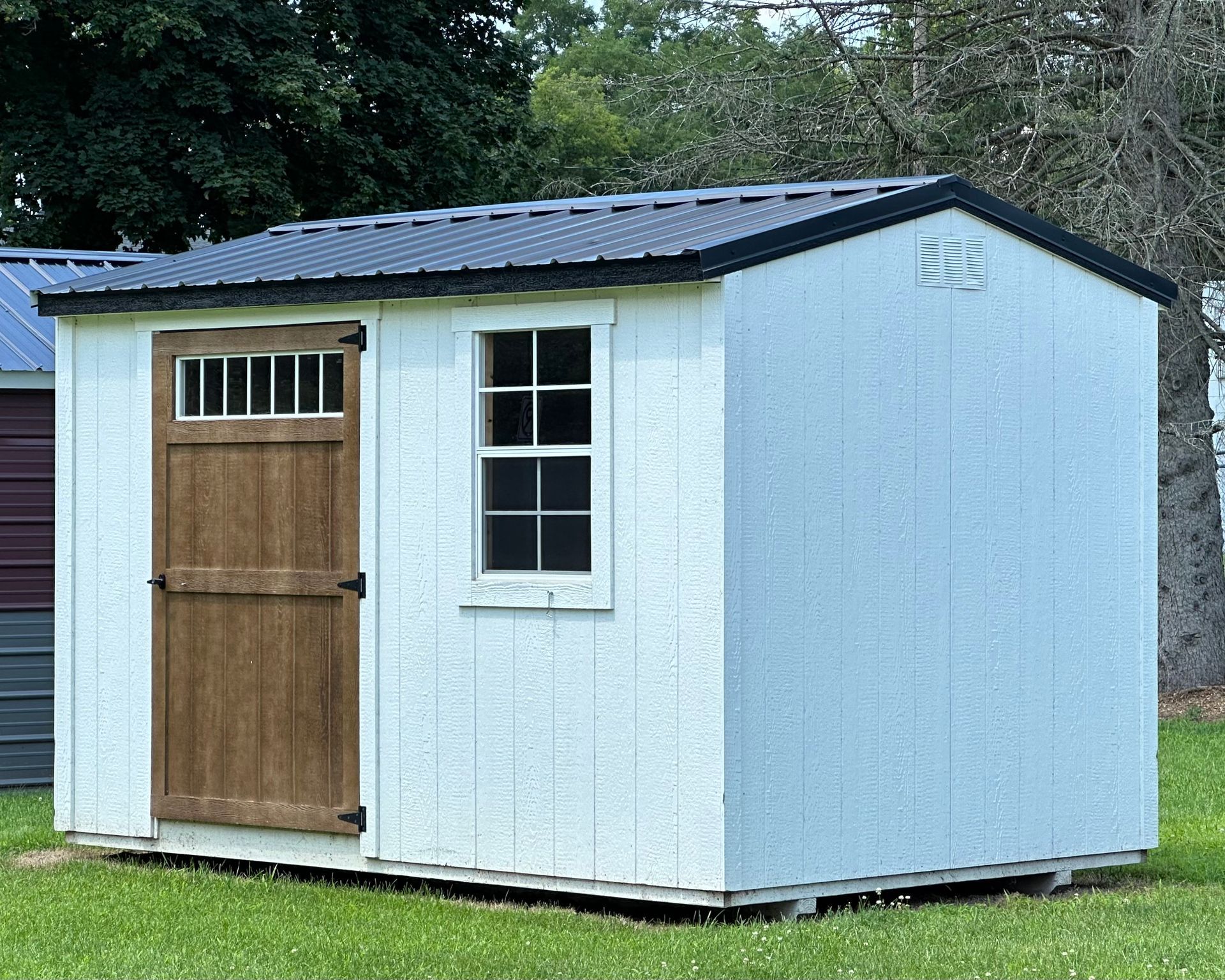 A white shed with a wooden door and window is sitting in the grass.