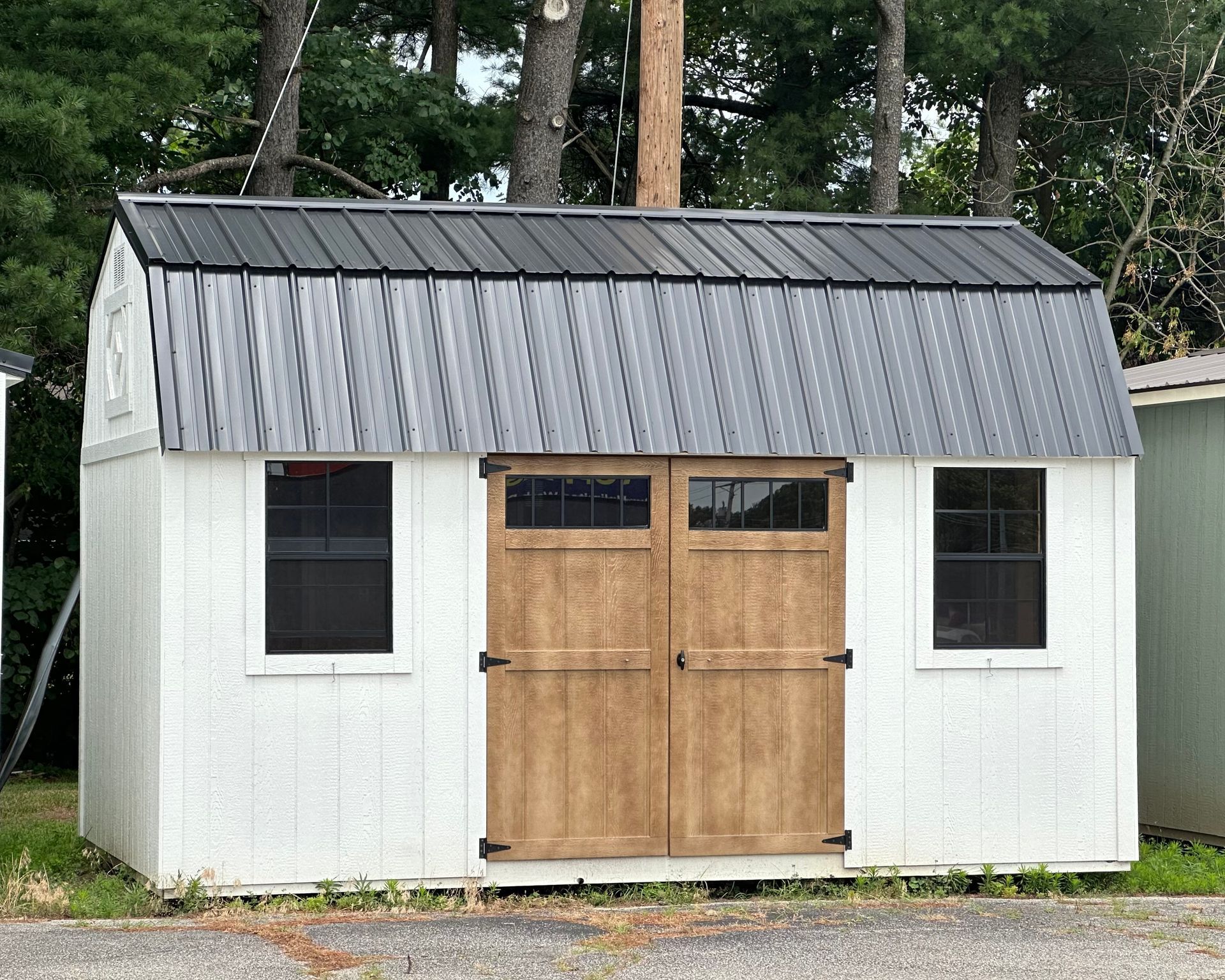 A white shed with a black roof and a wooden door.