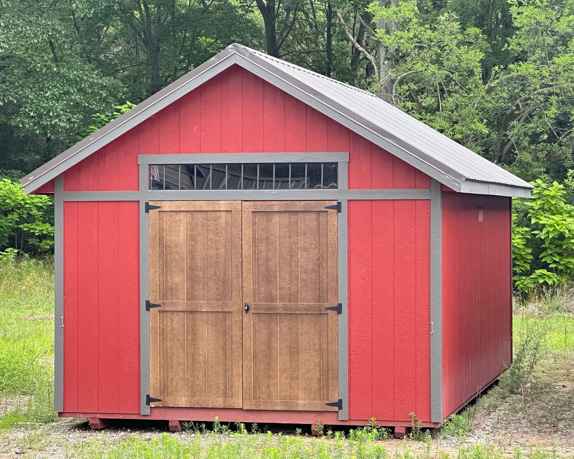 A red shed with a wooden door is sitting in the middle of a grassy field.