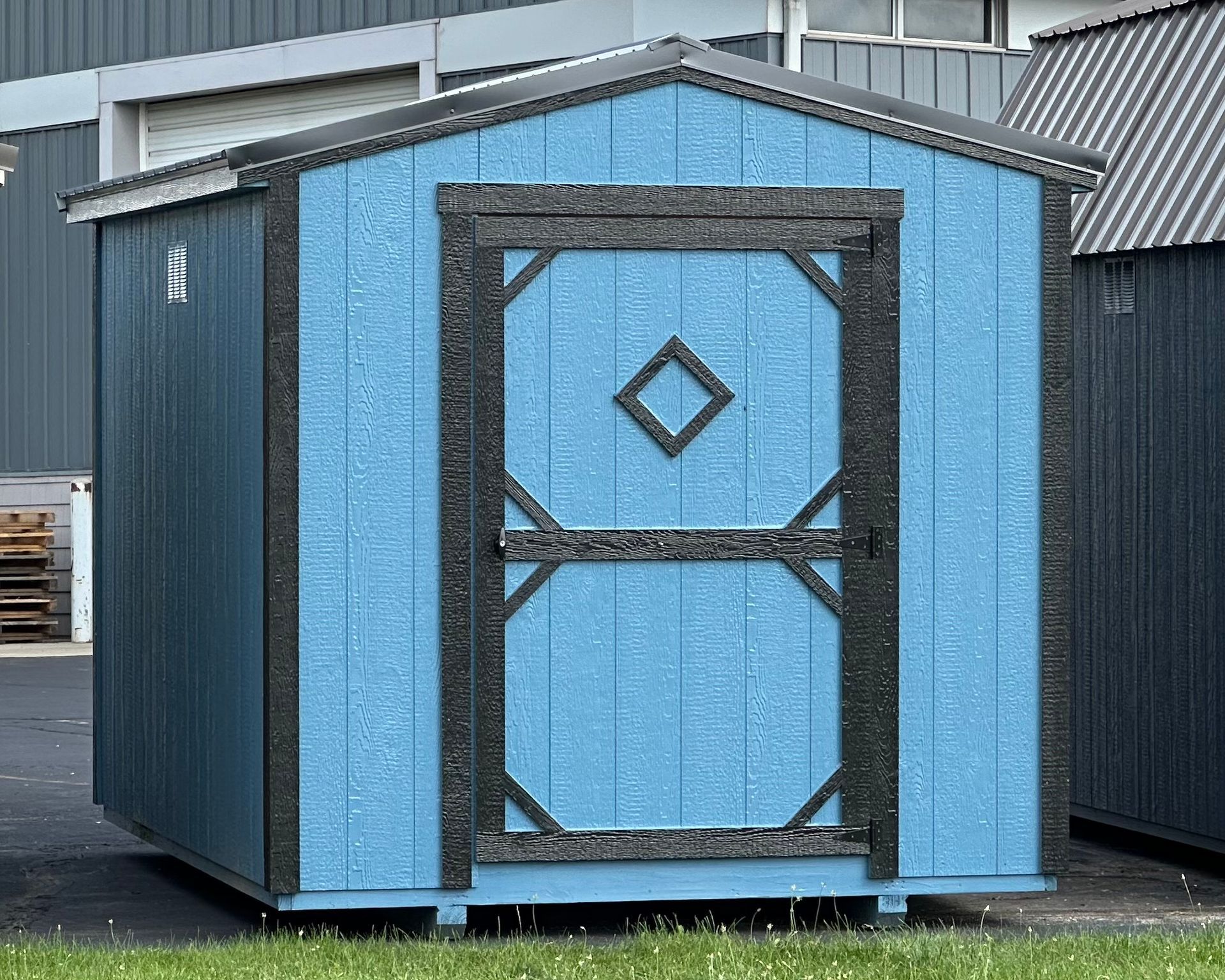 A blue shed with a diamond on the door is sitting in the grass.