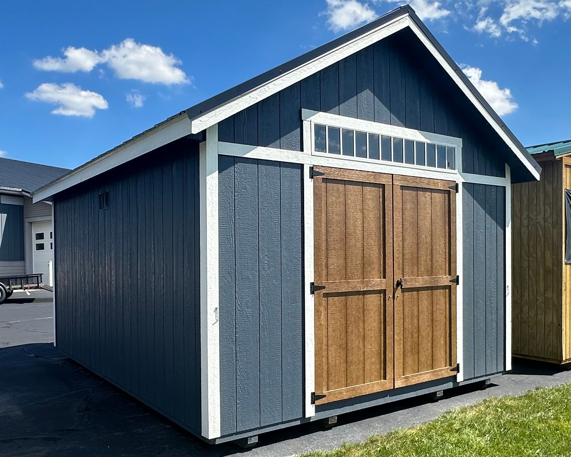 A blue and white shed with wooden doors is sitting in the grass.