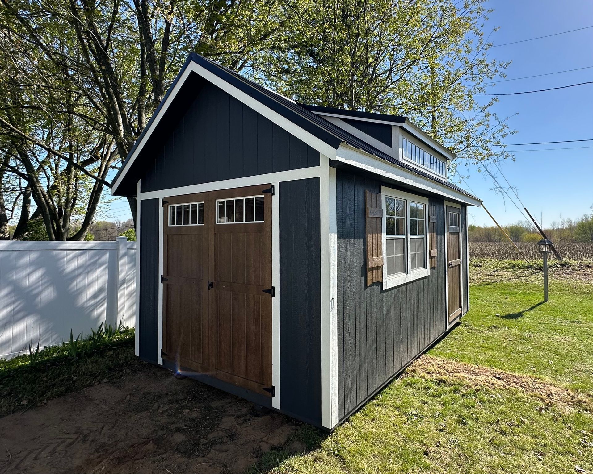 A small shed with a wooden door and windows is sitting in the middle of a grassy field.