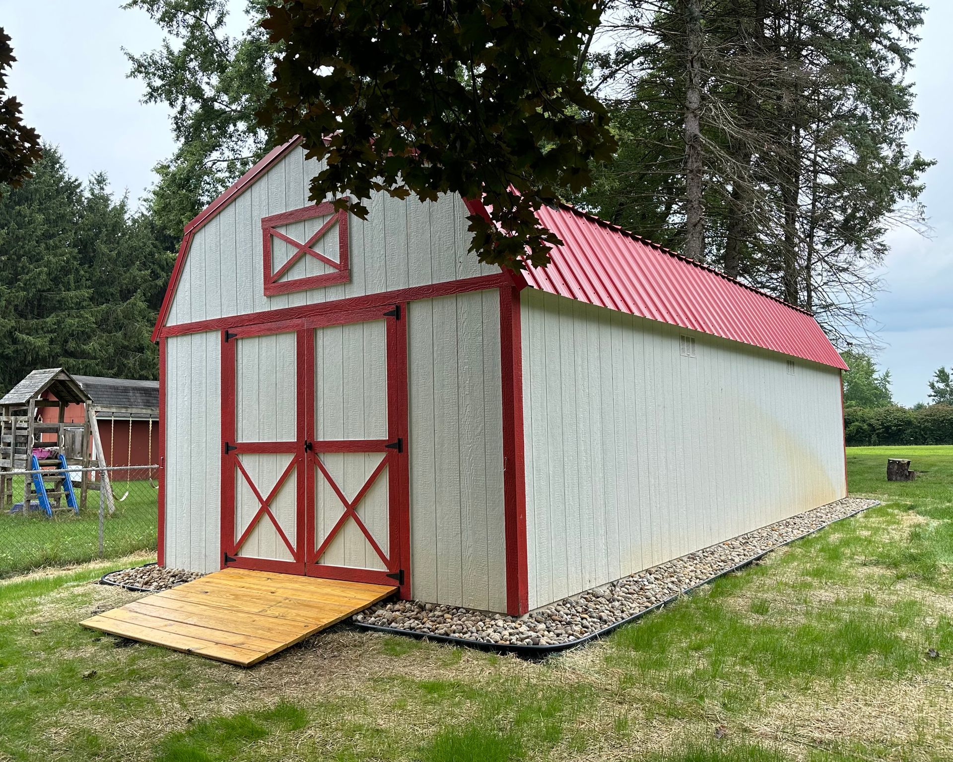 A white barn with a red roof is in the middle of a grassy field.