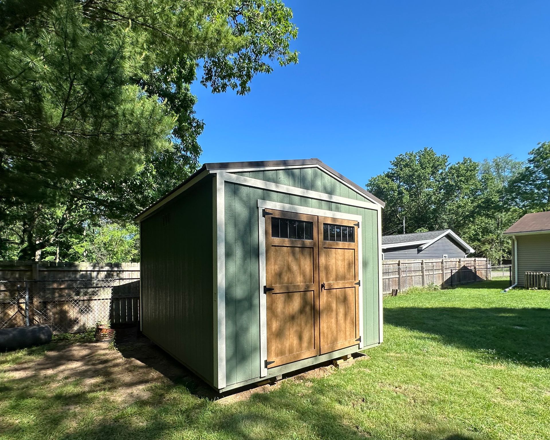 A green shed is sitting in the middle of a lush green yard.