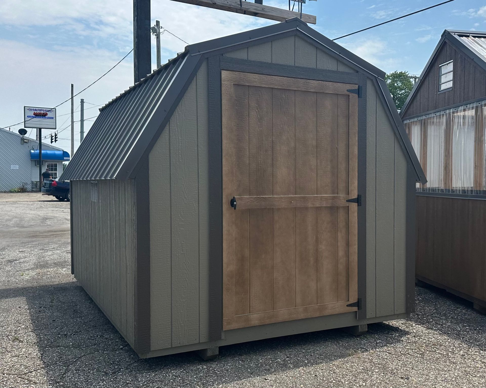 A small shed with a wooden door is sitting in a gravel lot.
