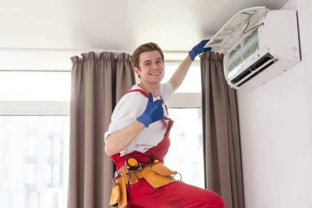 A professional HVAC contractor, with red overalls, smiles after completing an AC replacement job.