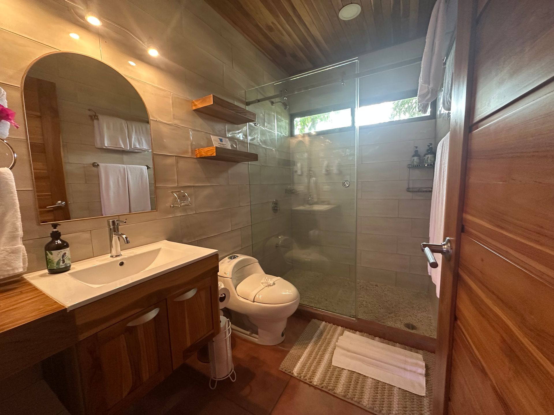 A bathroom with a toilet , sink , mirror and walk in shower.