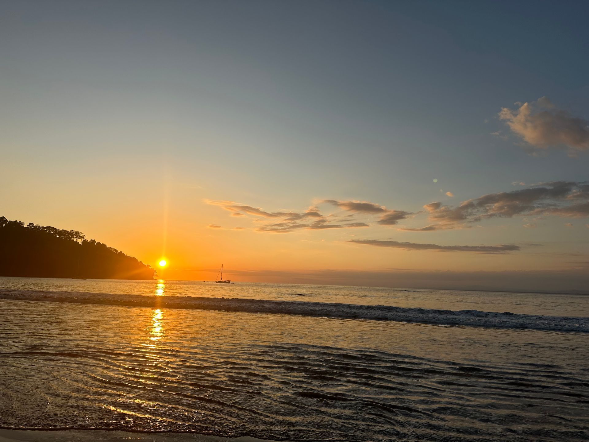 The sun is setting over the ocean with a boat in the distance.