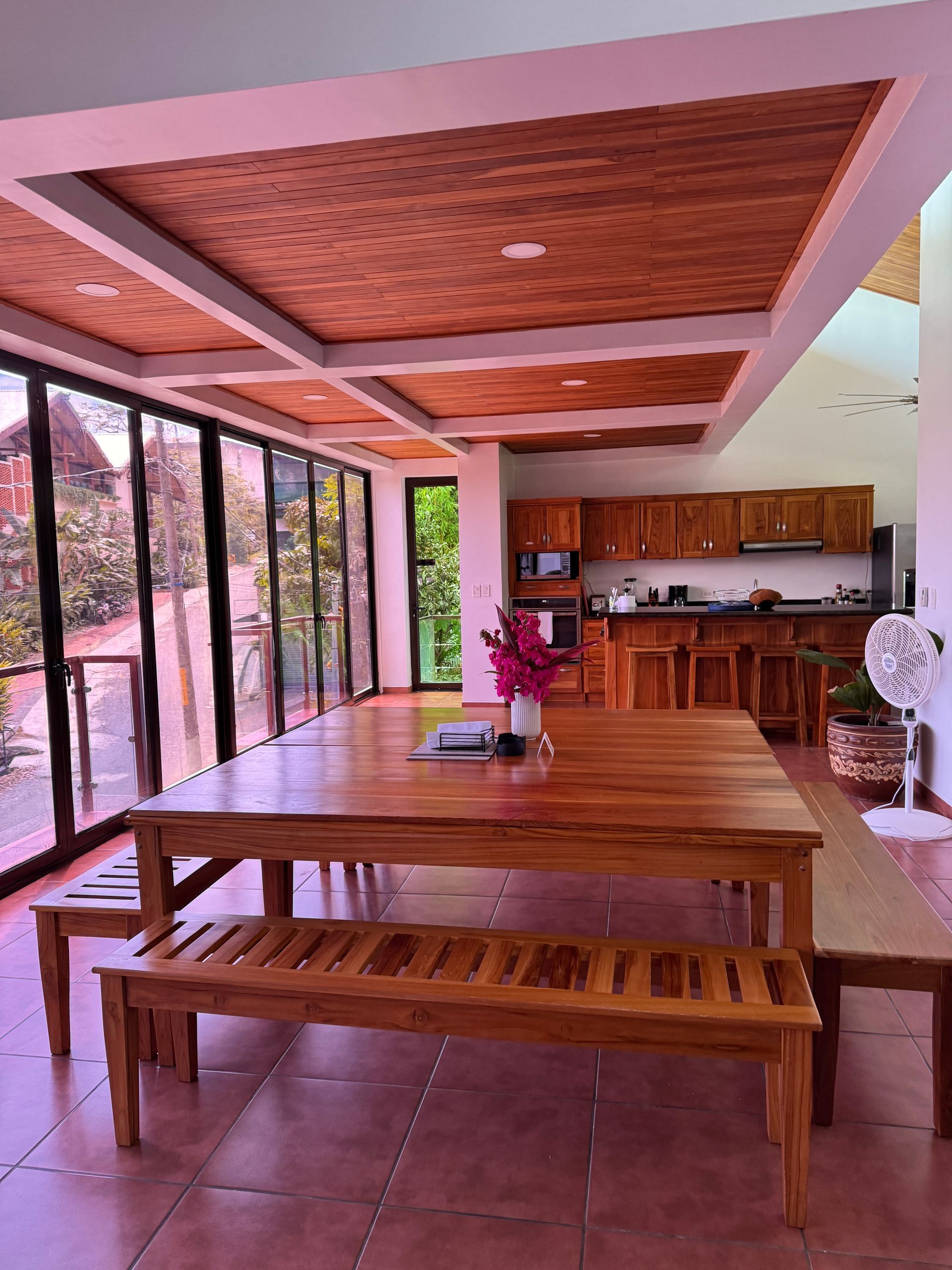 A large wooden table with benches in a room with a lot of windows.