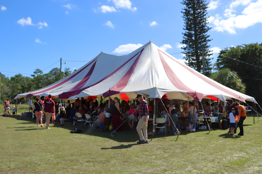 A large tent with red and white stripes, set up outdoors with a food service trailer next to it.