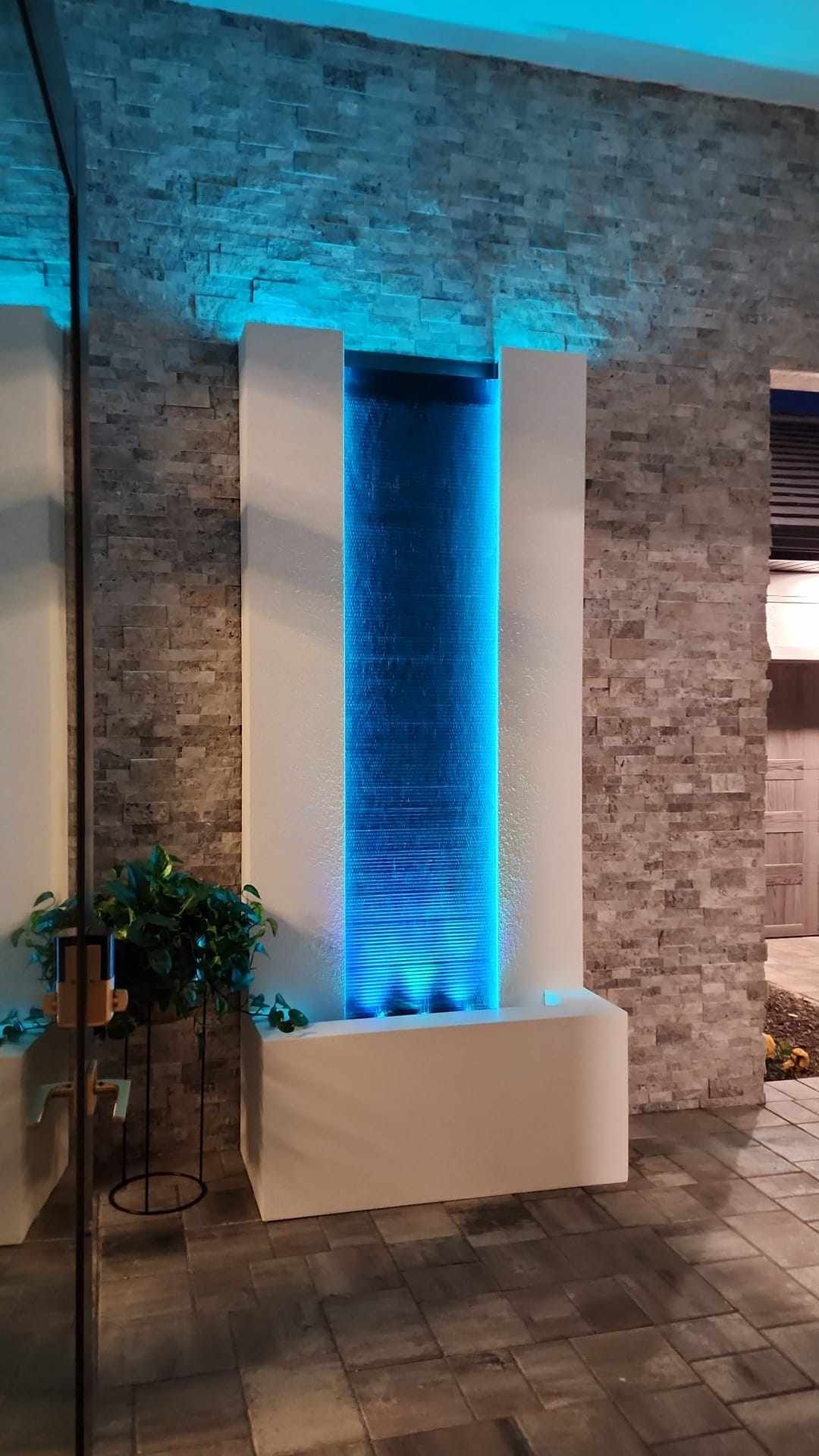 Water fountain with blue LED lights, in front of a stone wall