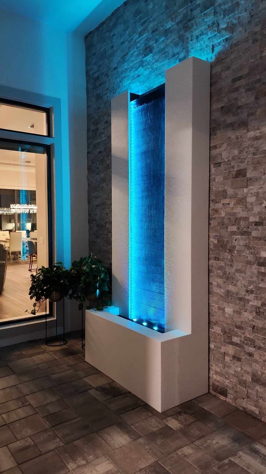 Modern outdoor fountain with blue lighting, set against textured stone walls