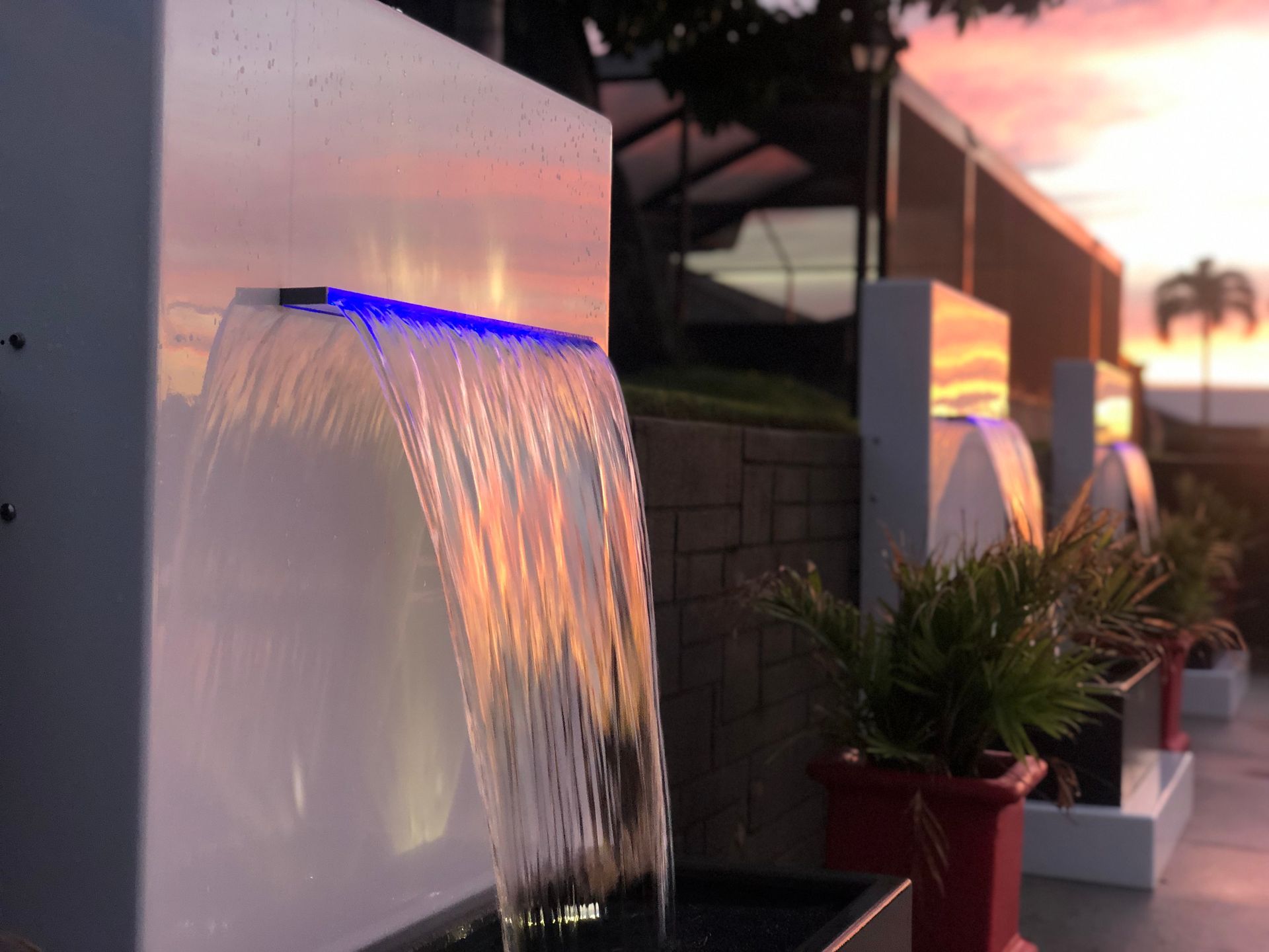 Waterfall fountain with blue light, red pots, and a sunset