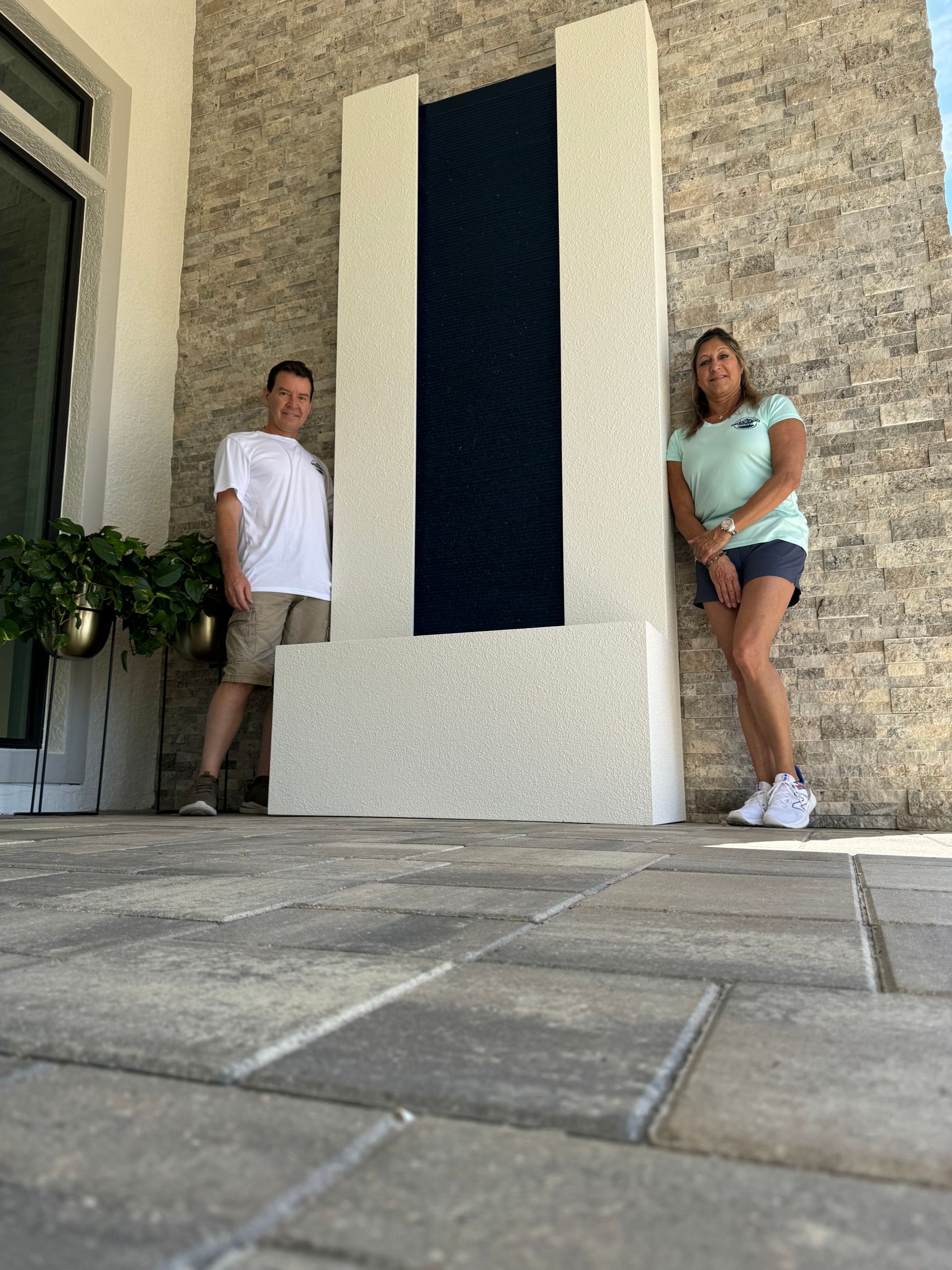 Two people pose next to a large white and blue outdoor water feature