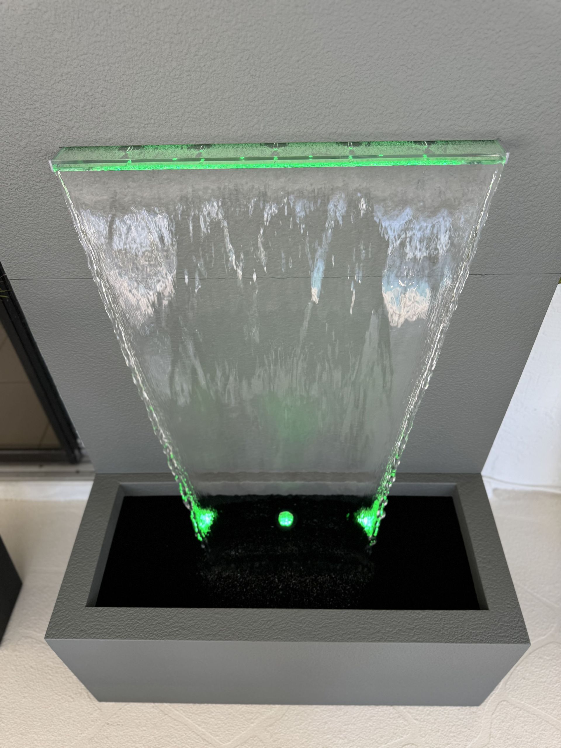 Water fountain with green LED lights, cascading from a glass top into a grey basin