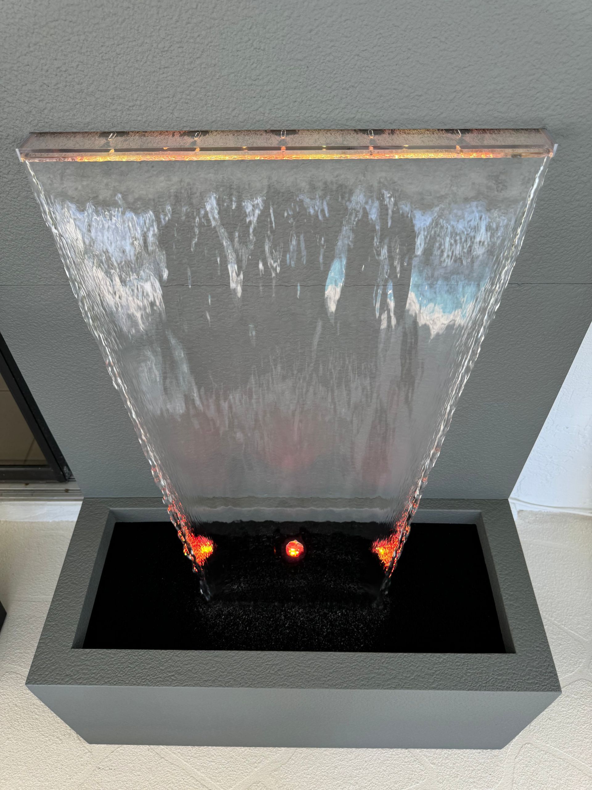 Water fountain with a rectangular basin and a cascading water sheet, lit with orange lights