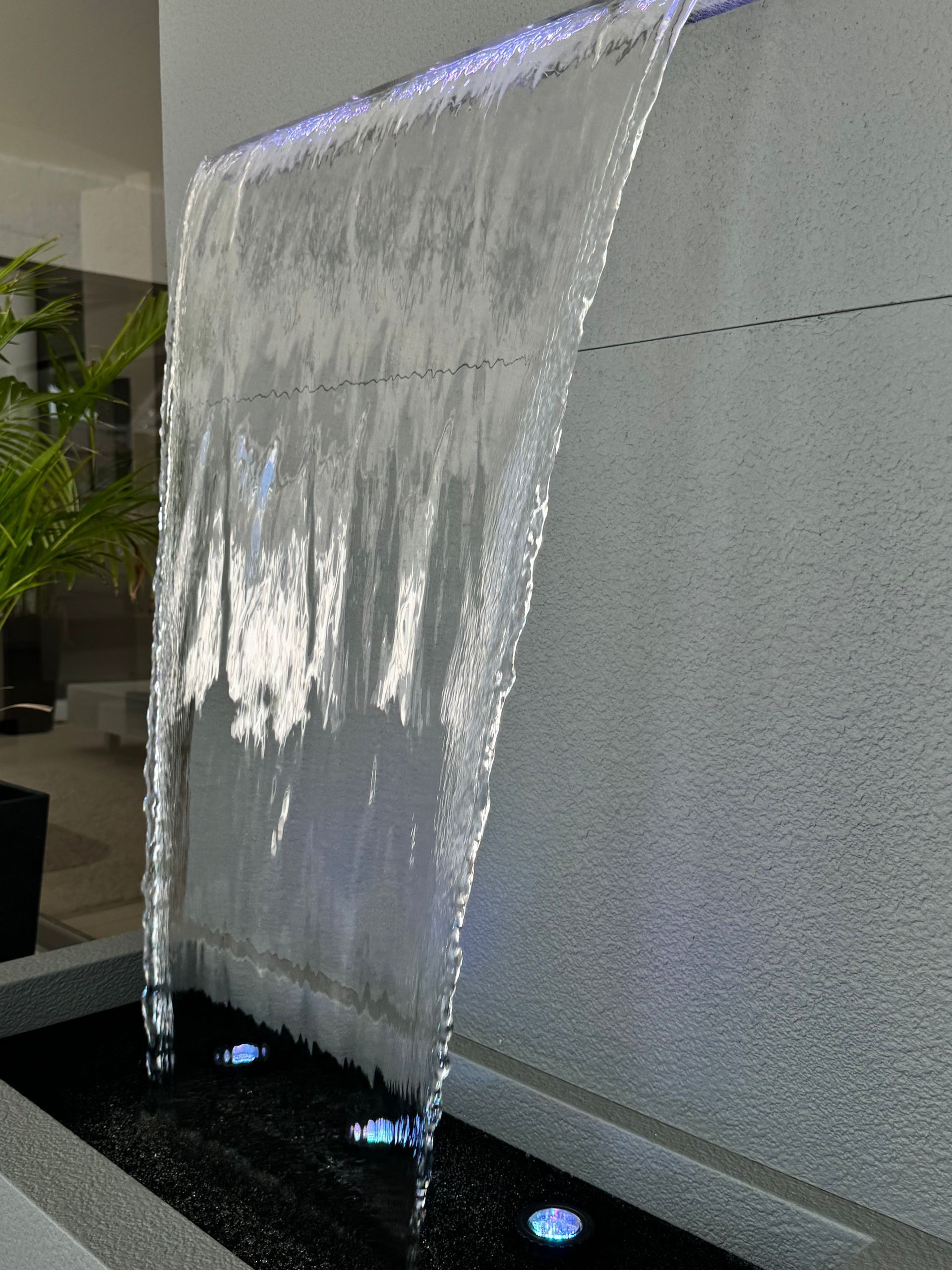 Water fountain against a gray wall, clear water cascading into a dark basin with blue lights