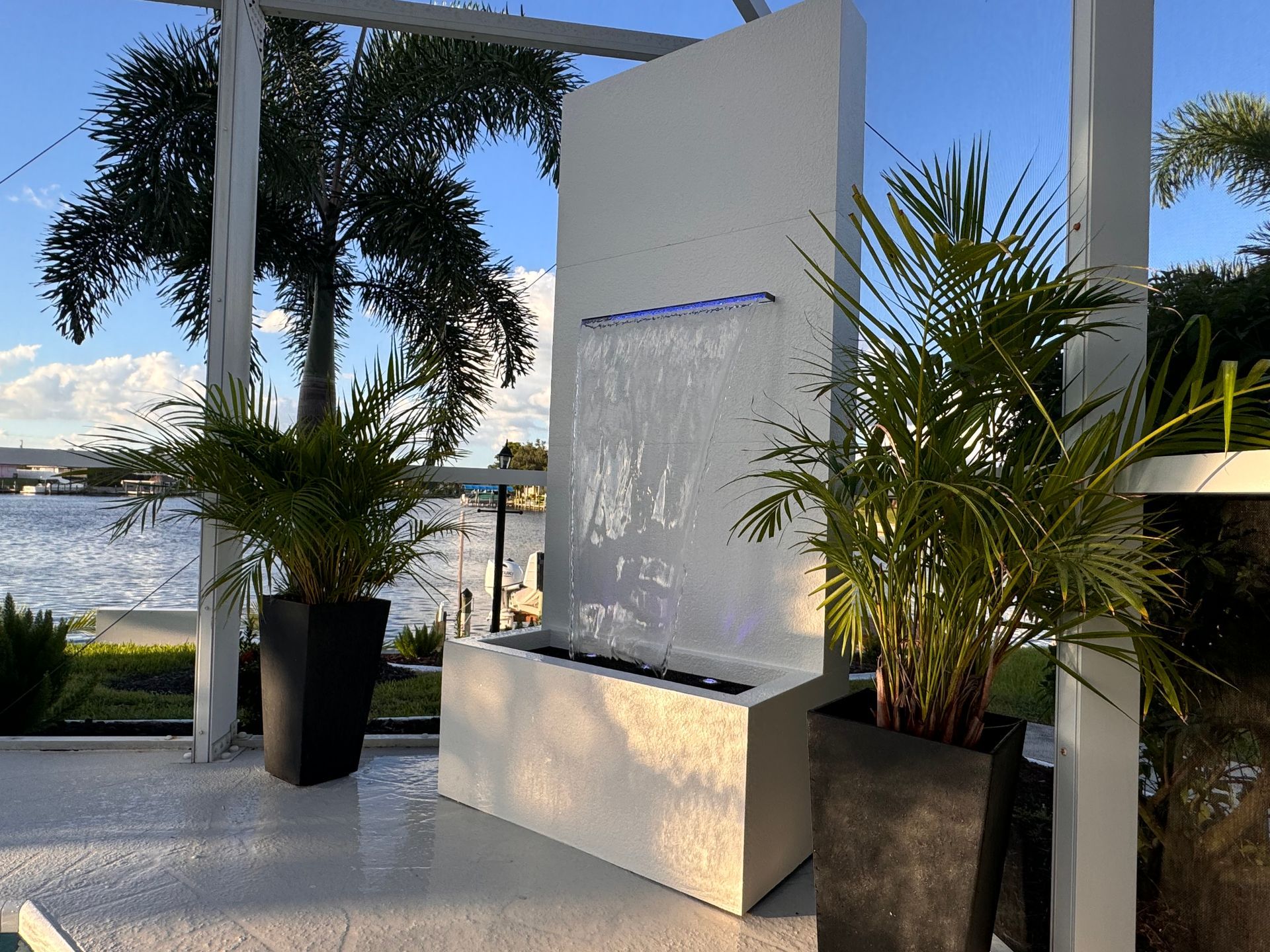 White waterfall fountain with plants on patio by water