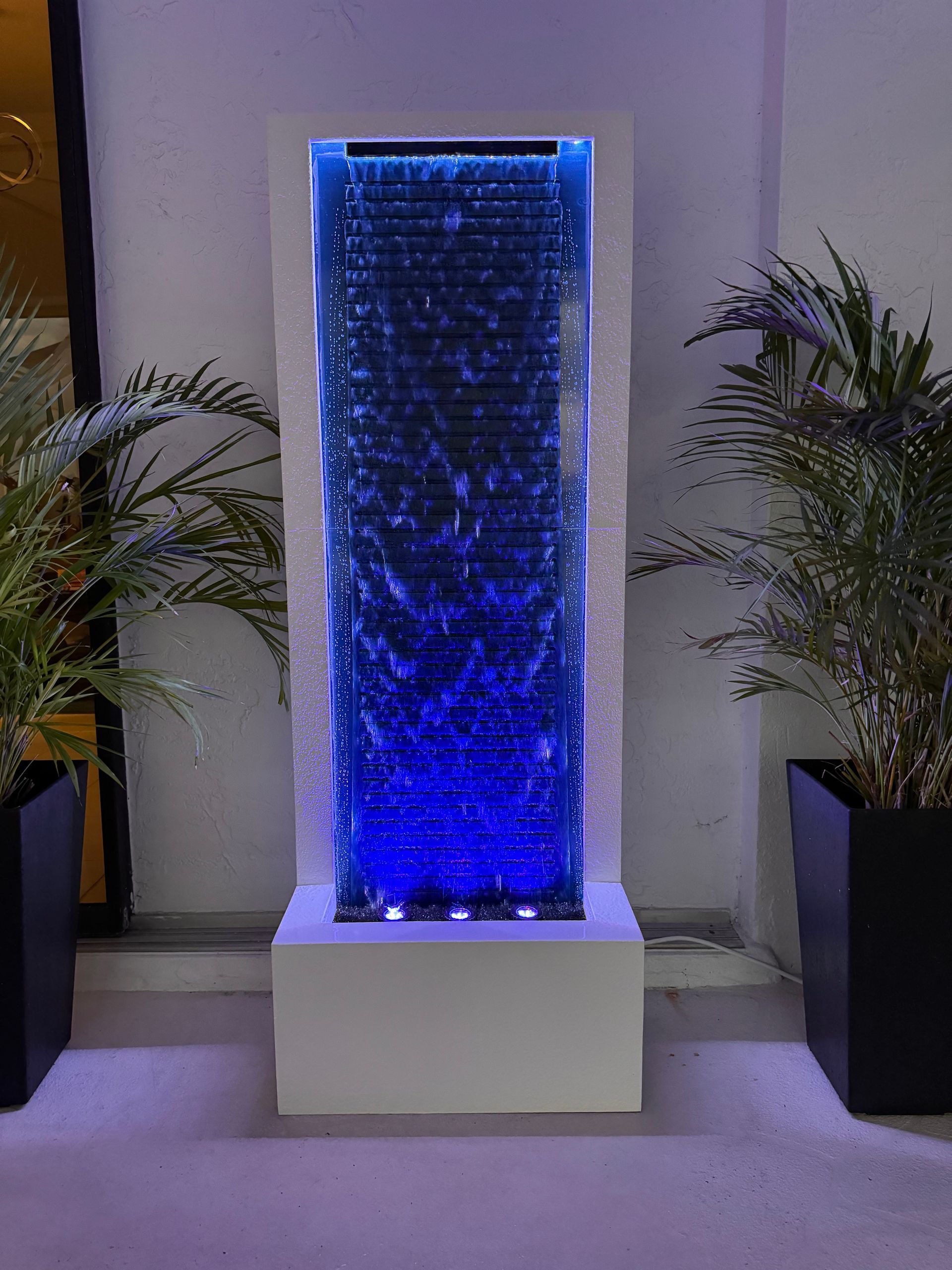 Tall water fountain with blue illuminated bubbles, flanked by potted plants