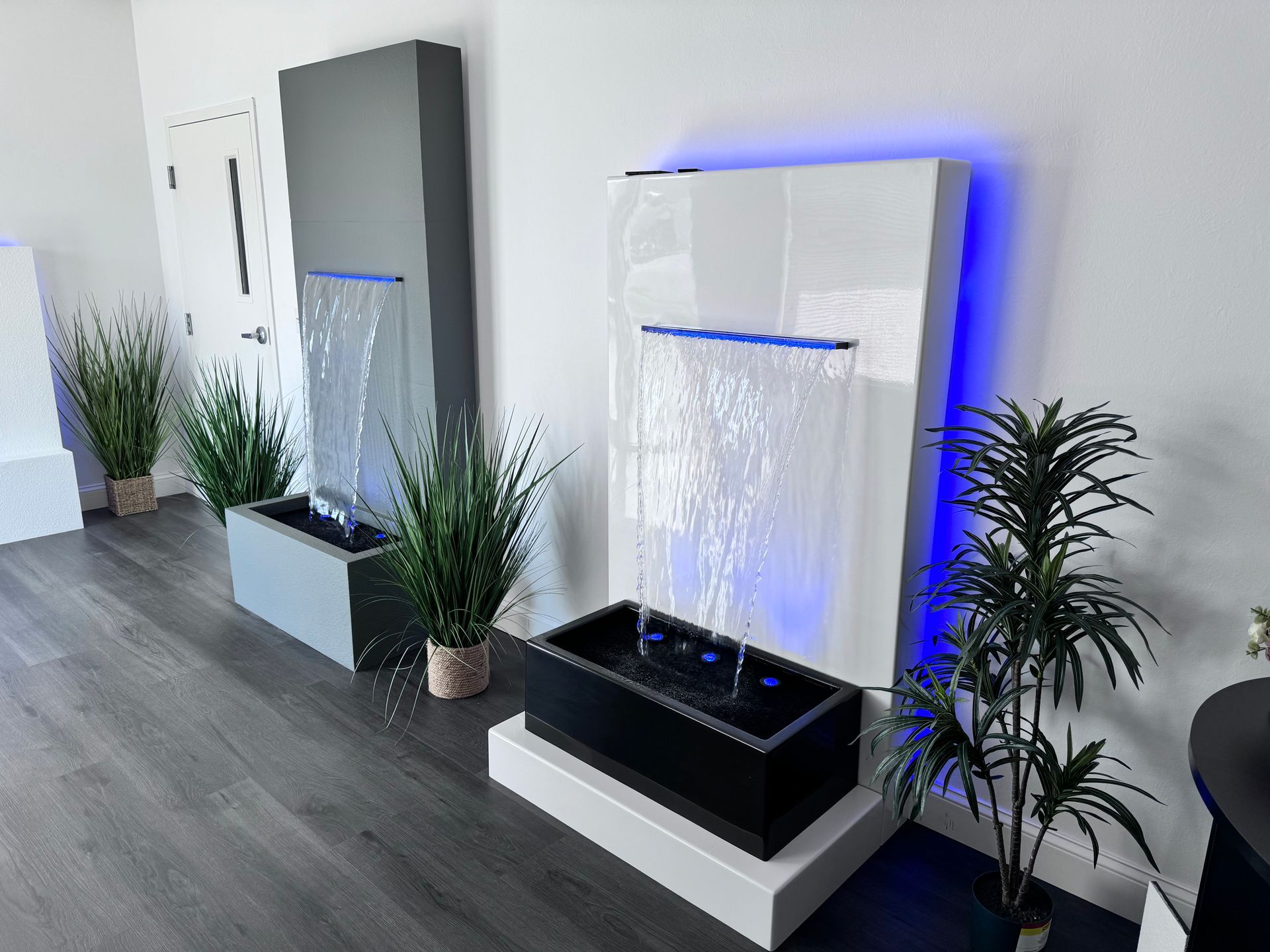 Two modern wall fountains with water cascading into rectangular basins, plants flanking each