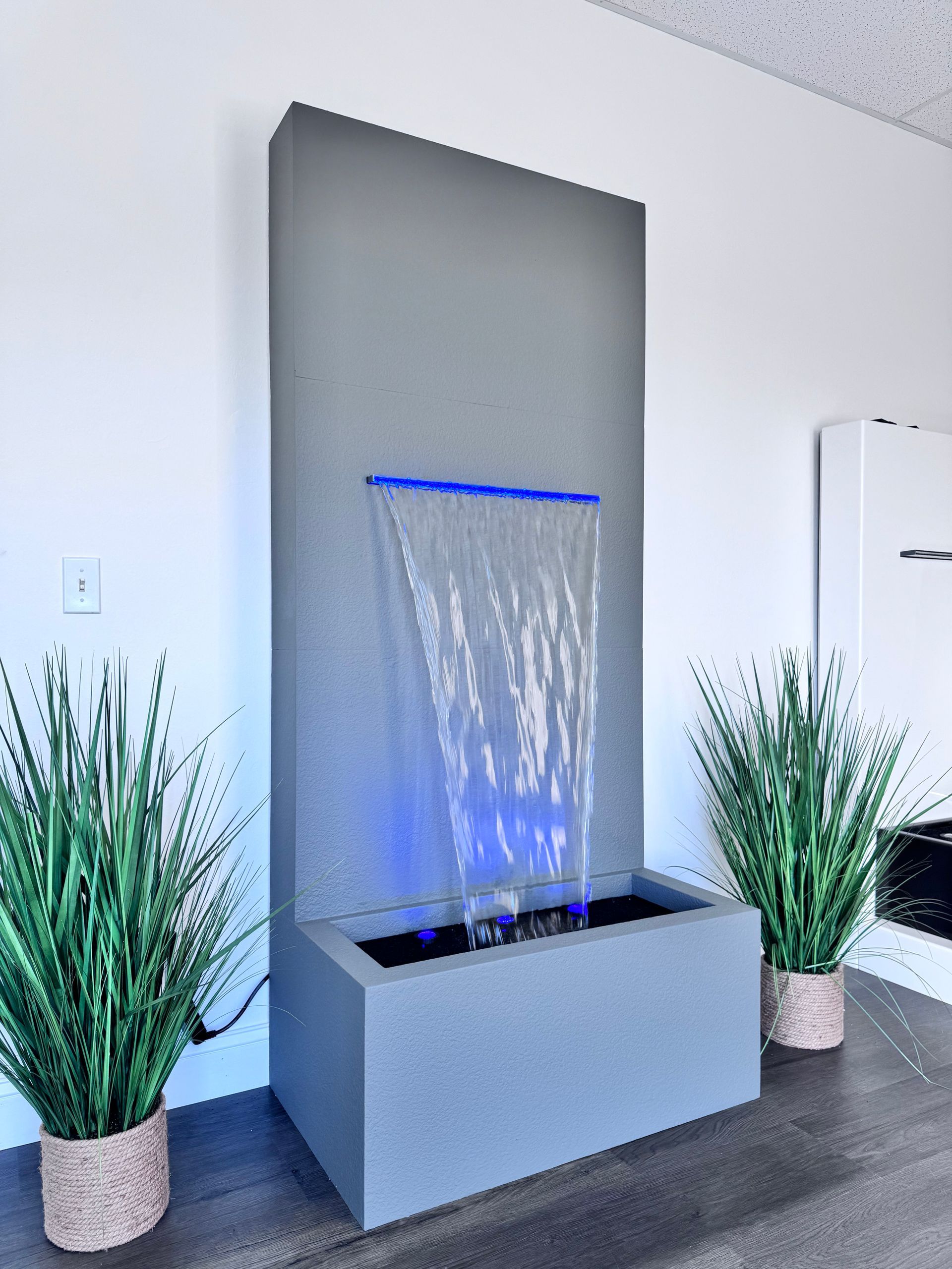 Indoor water fountain with blue LED light on a gray wall