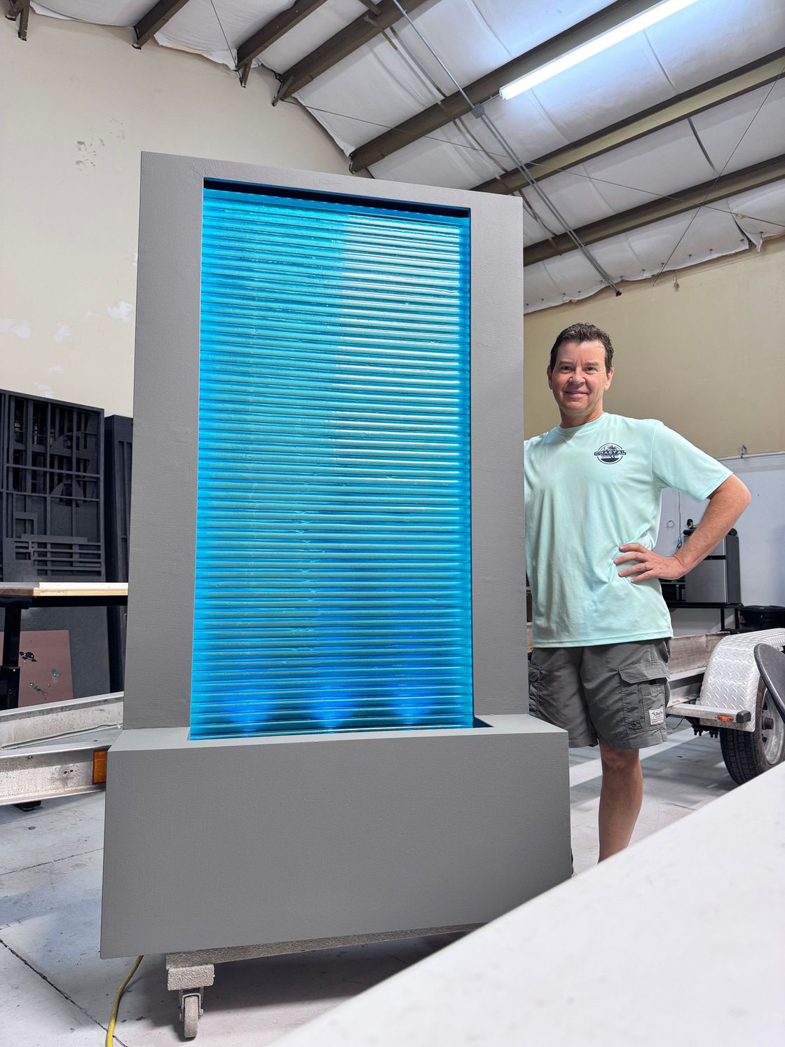 Man stands beside a tall, gray, illuminated water fountain with blue water flowing