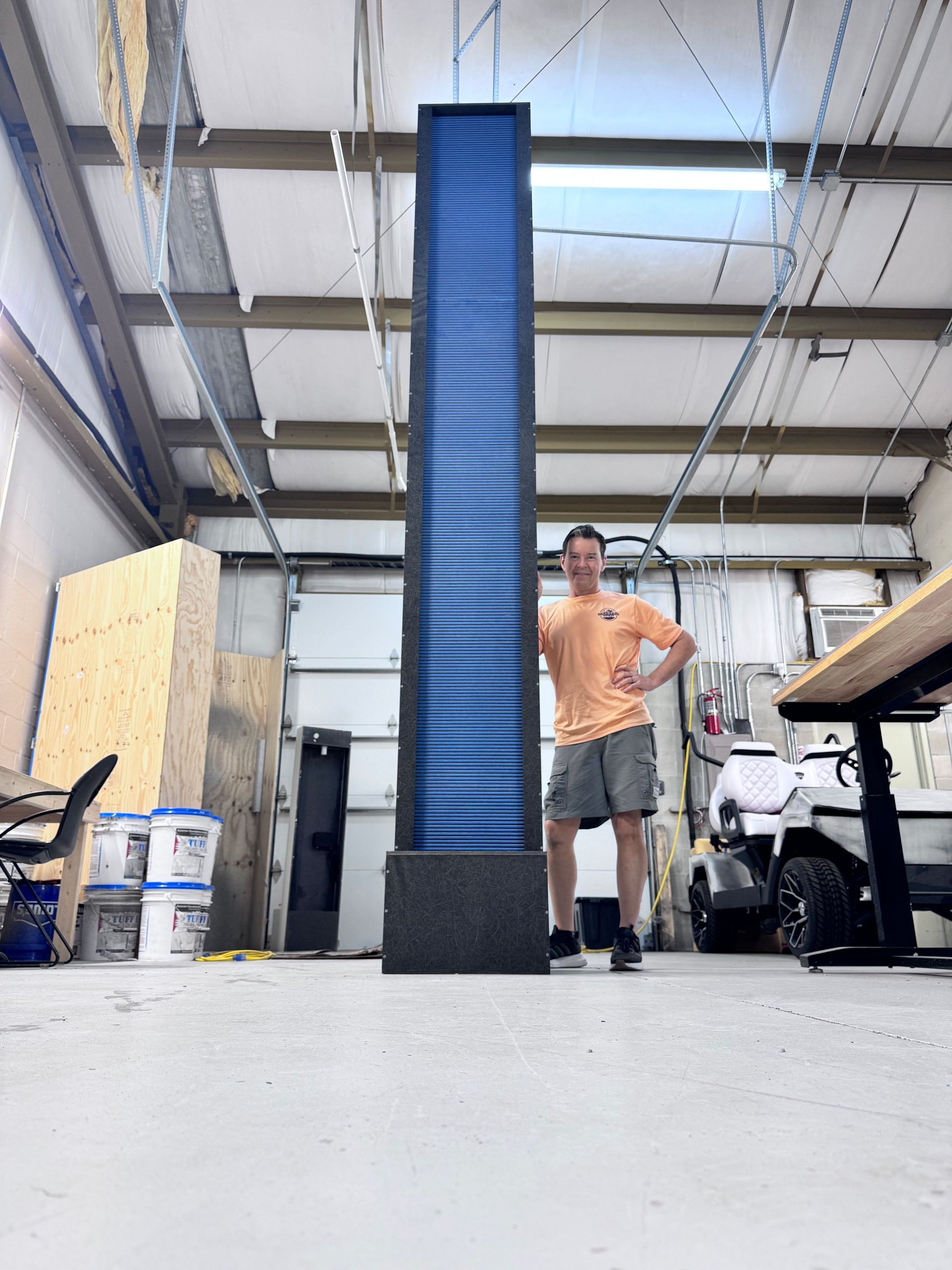 Man standing beside a tall, dark blue light sculpture inside a workshop