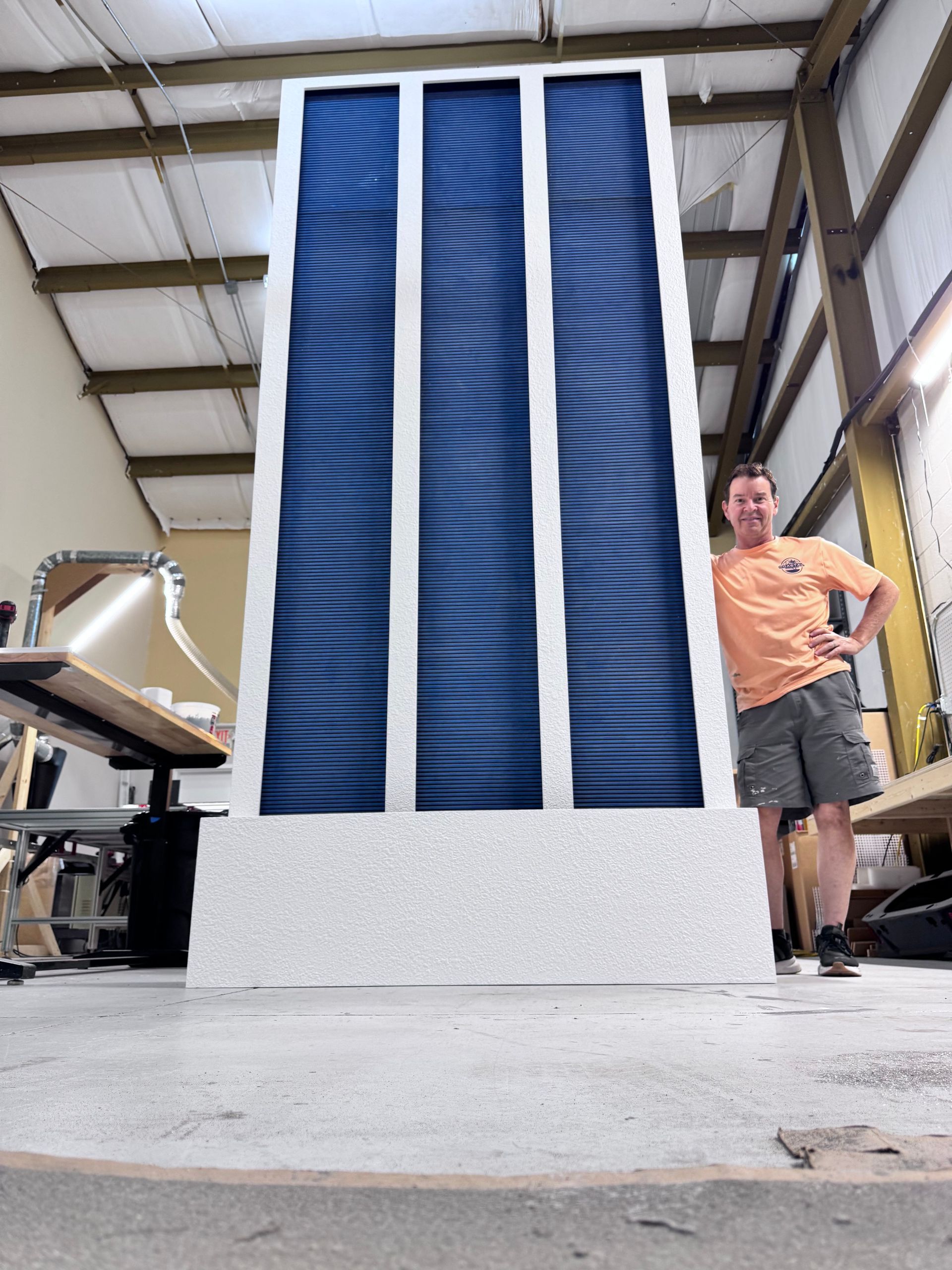 Man stands next to a large, blue-paneled structure with white borders inside a building
